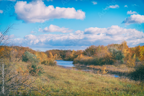 Autumn landscape. Blue sky with clouds, small river, orange leaves on trees