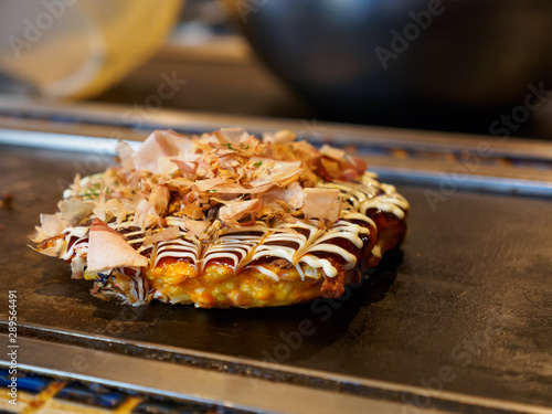 Closeup macro detail of a freshly cooked Okonomiyaki with Katsuobushi, dried fish flakes, sauce, and mayonnaise, on a Teppan grill. Shallow focus. Dotonbori, Osaka, Japan. Travel and cuisine.
