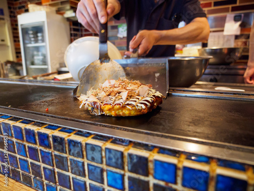 Closeup of a Okonomiyaki cooked on a teppan grill, topped with Katsuobushi fish flakes, sauce, and mayonnaise. Shallow focus. Dotonbori, Osaka, Japan. Travel and cuisine. photo