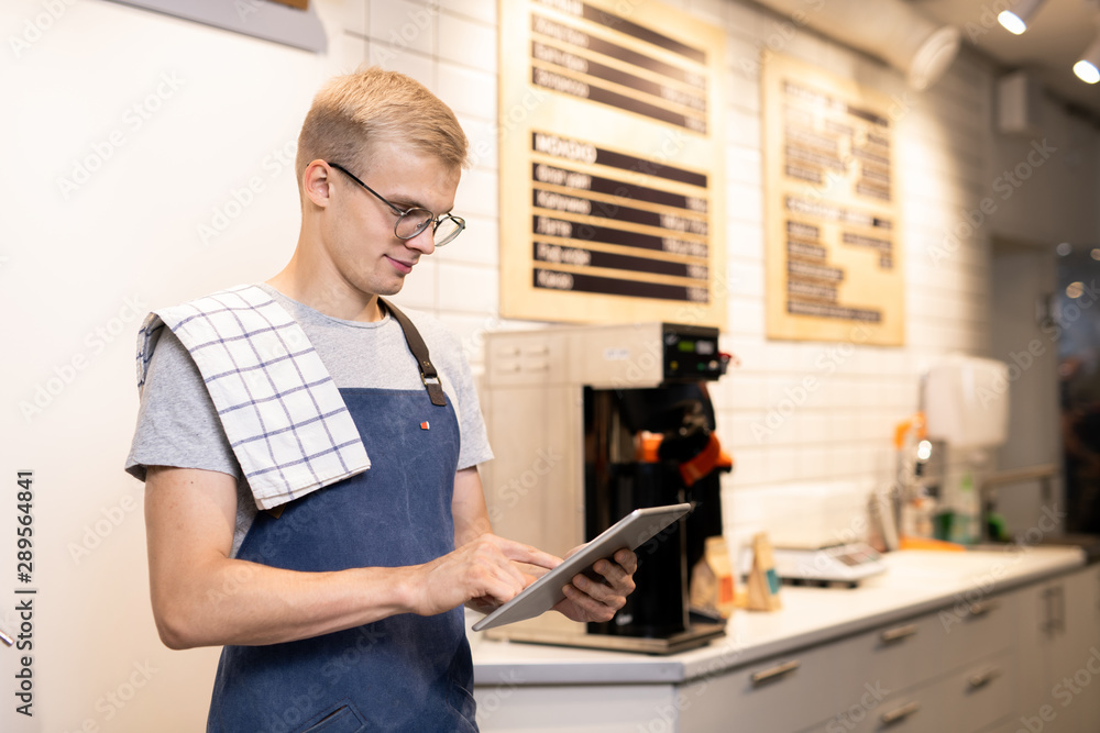 Young barista in workwear using digital tablet to enter new menu of drinks Young barista in workwear using digital tablet to enter new menu of drinks