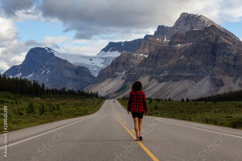 Girl walking down a scenic road in the Canadian Rockies during a vibrant summer evening. Taken in Icefields Parkway, Banff National Park, Alberta, Canada.