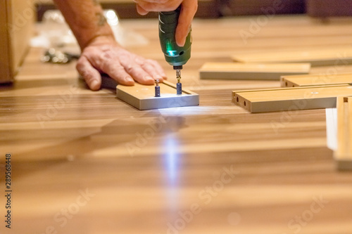 Wooden furniture assembling, woodworker screwing screws using a cordless Assembling furniture from chipboard, using a cordless screwdriver furniture, home and moving concept