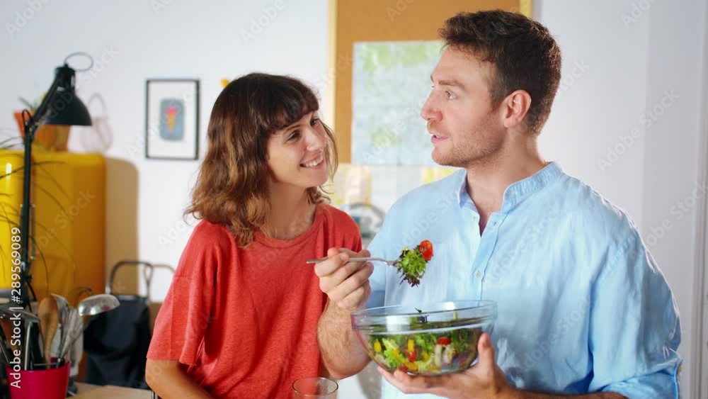 Enamored girl joking at trifle with smiling boyfriend eating fresh salad at home kitchen, spending time together chatting during lunch having fun organic food content positive emotions of couple Enamored girl joking at trifle with smiling boyfriend eating fresh salad at home kitchen, spending time together chatting during lunch having fun organic food content positive emotions of couple