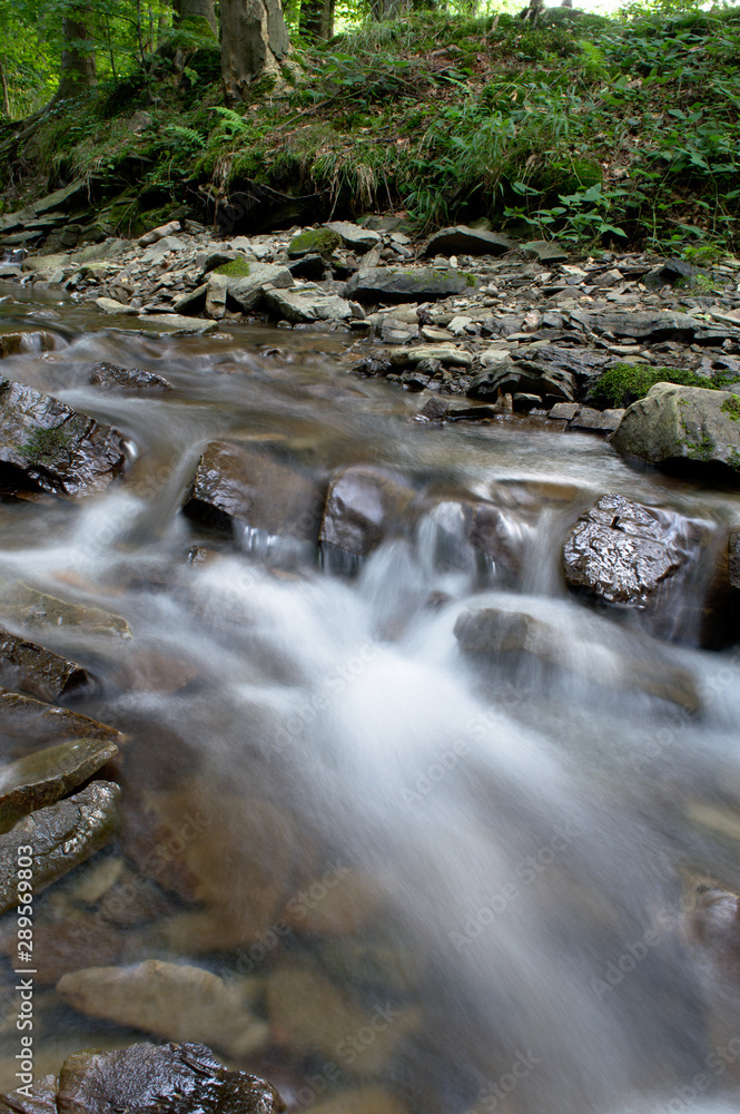 Small waterfall in the mountain forest with stones, long exposure