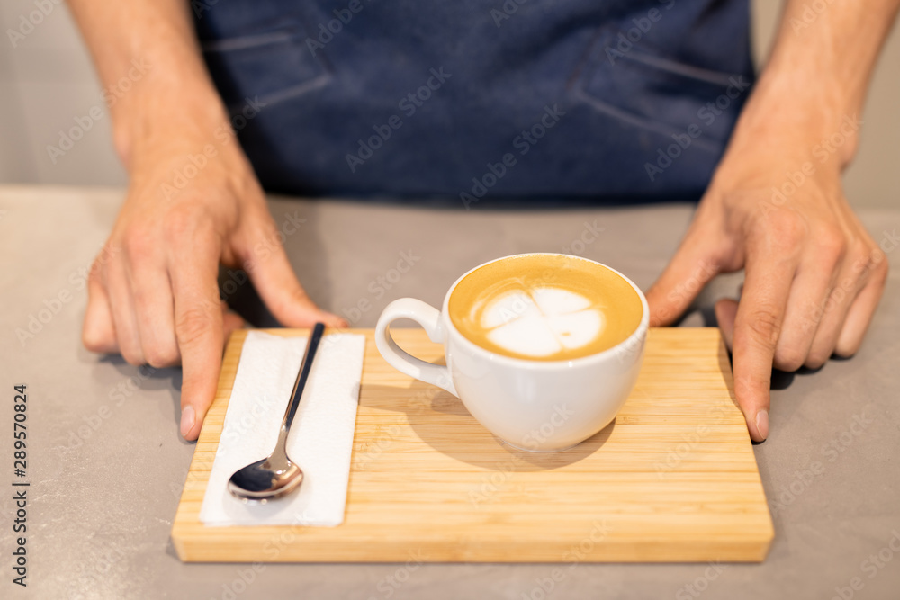 Porcelain cup of cappuccino and small spoon with paper napkin on wooden tray Porcelain cup of cappuccino and small spoon with paper napkin on wooden tray