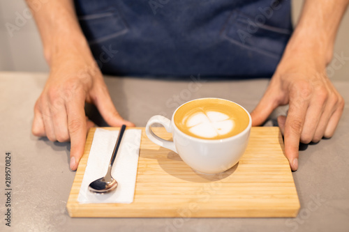 Porcelain cup of cappuccino and small spoon with paper napkin on wooden tray