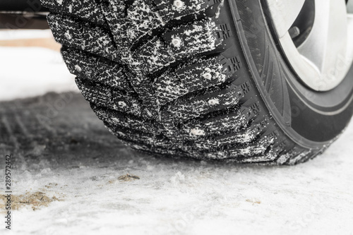 Car wheel on a slippery snowy winter road. Deep tread of winter studded tires close-up.