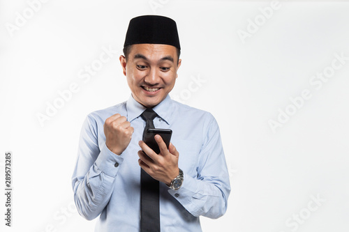 Asian male with songkok looking at his phone photo