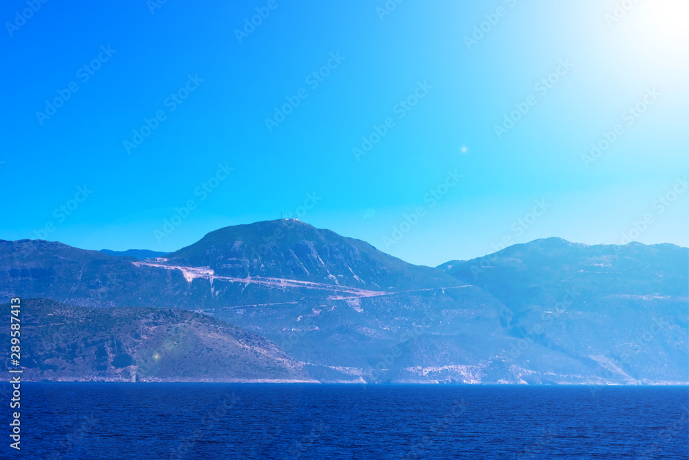 Seascape with mountains, calm blue Meditarrenian sea and bright sunbeams, summer season of tourists, vacation on sunny islands