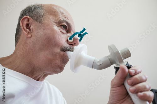 Senior hispanic man man testing breathing function by spirometry. Diagnosis of respiratory function in pulmonary disease photo
