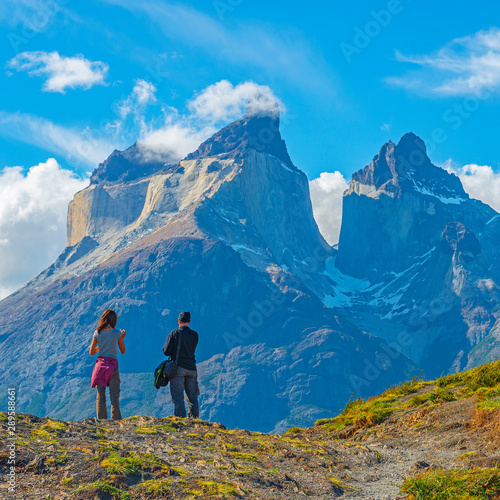Two tourist, a man and a woman, looking upon a viewpoint of the Andes peaks of Cuernos del Paine, Torres del Paine national park, Puerto Natales, Patagonia, Chile.