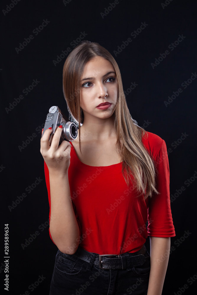 Beautiful girl with oldstyle camera posing in red shirt on black background.