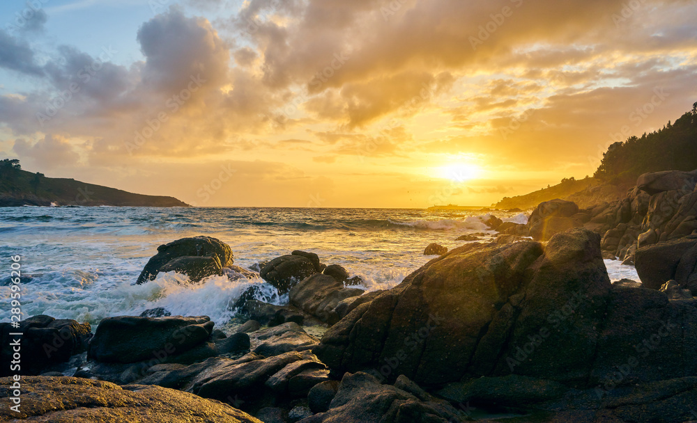 Sunset of the sea with rocks and mountain in the background. Beach and sea water with long exposure.