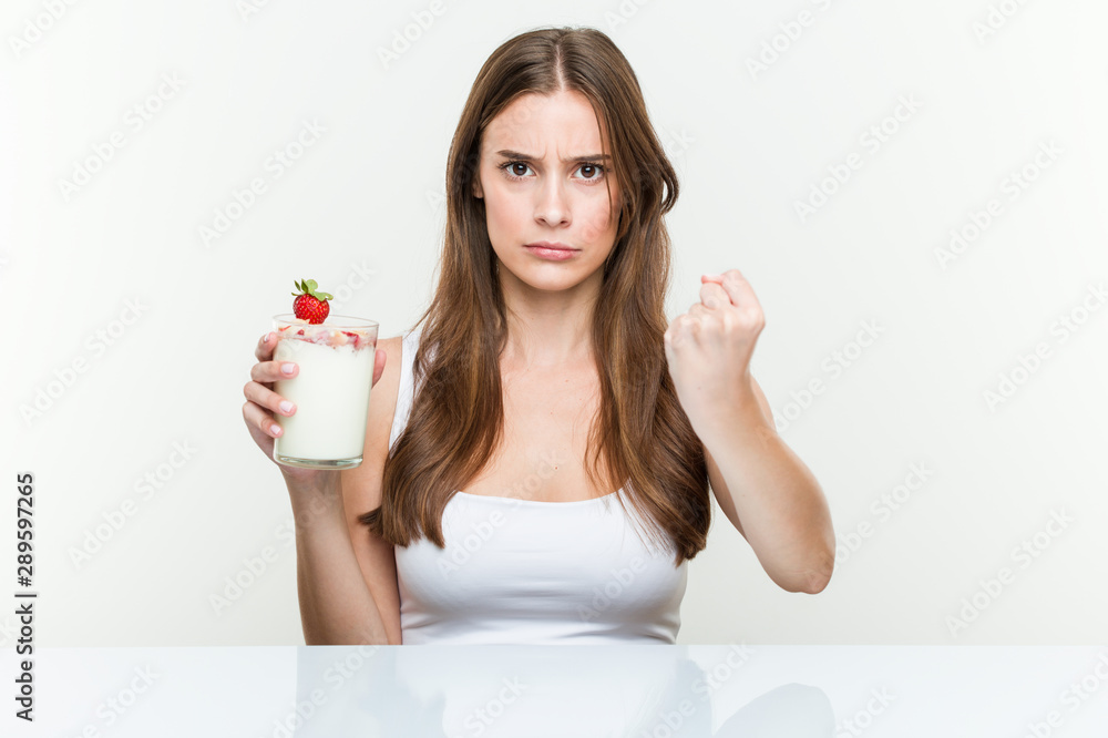 Young caucasian woman holding a smoothie showing fist to camera, aggressive facial expression. Young caucasian woman holding a smoothie showing fist to camera, aggressive facial expression.