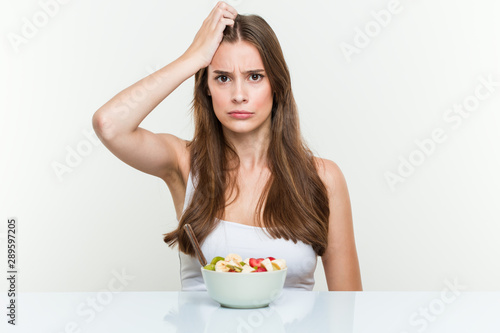 Young caucasian woman eating fruit bowl being shocked, she has remembered important meeting.