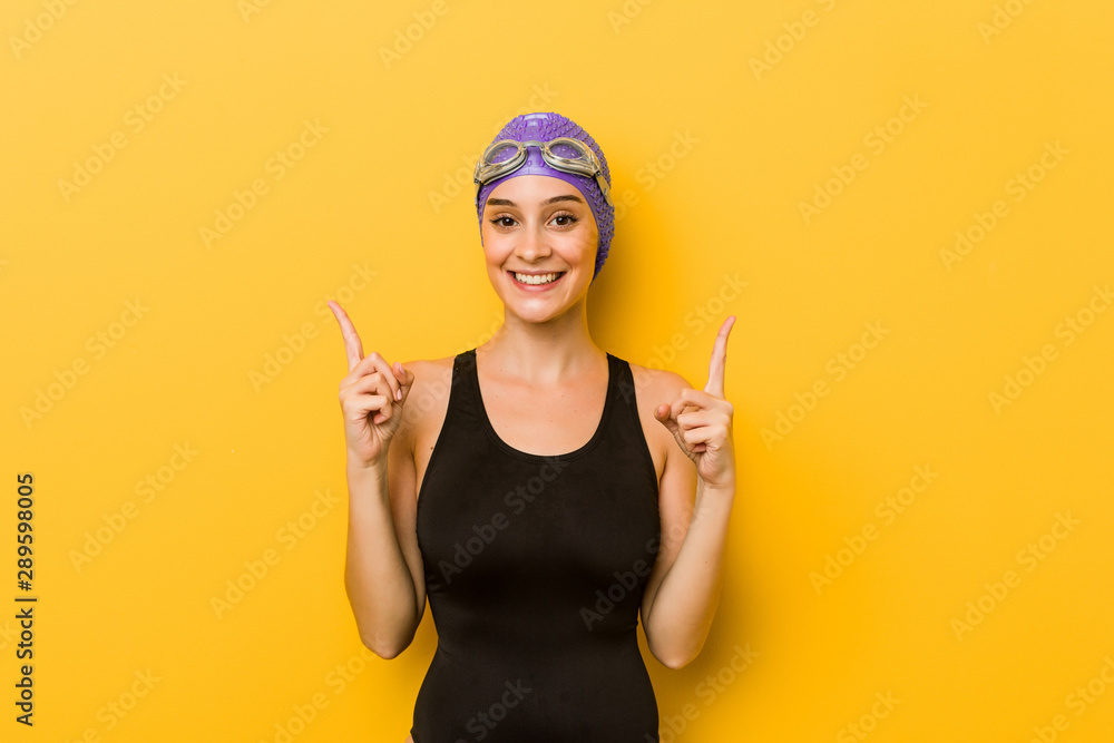Young swimmer caucasian woman indicates with both fore fingers up showing a blank space. Young swimmer caucasian woman indicates with both fore fingers up showing a blank space.
