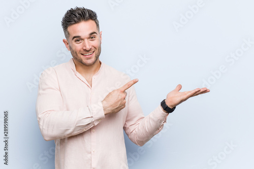 Young handsome cool man excited holding a copy space on palm.