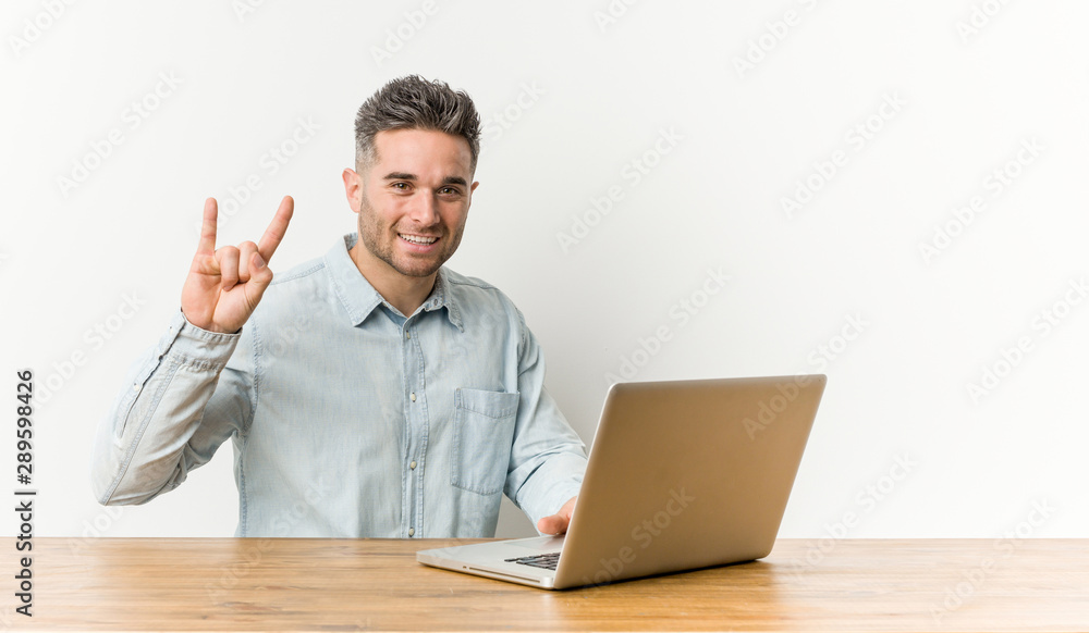 Young handsome man working with his laptop showing a horns gesture as a revolution concept. Young handsome man working with his laptop showing a horns gesture as a revolution concept.