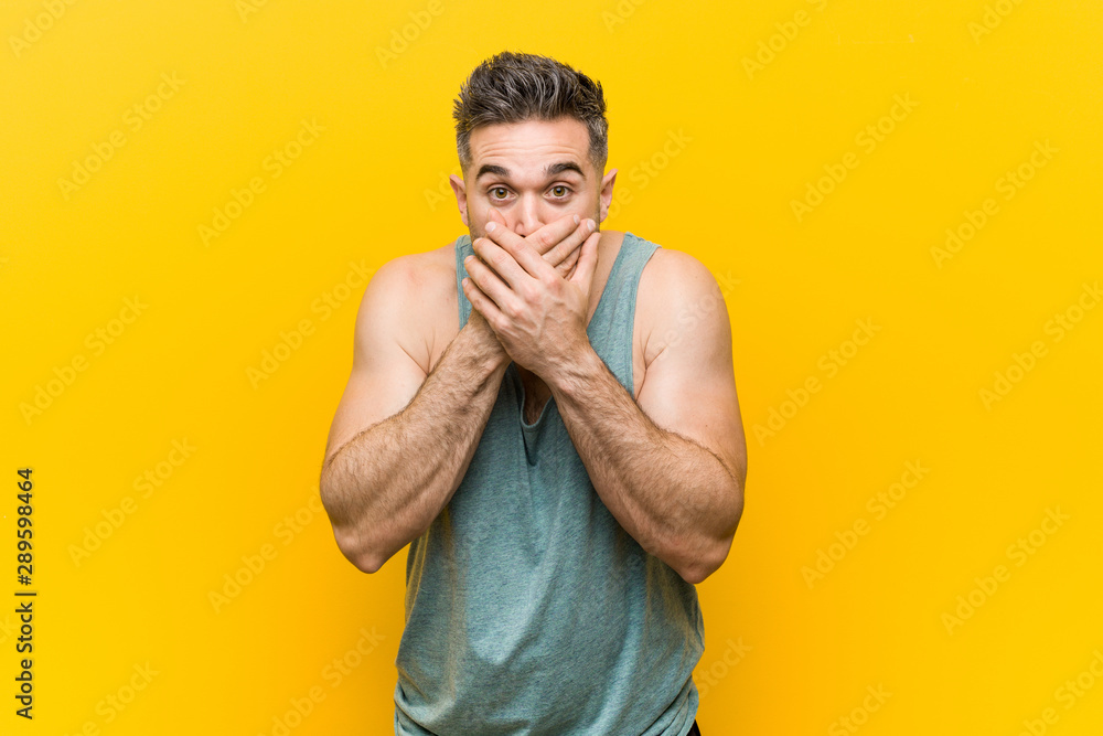 Young fitness man against a yellow background shocked covering mouth with hands. - obrazy, fototapety, plakaty 
