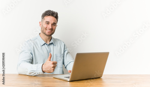 Young handsome man working with his laptop smiling and raising thumb up