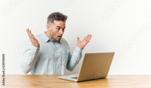 Young handsome man working with his laptop surprised and shocked.