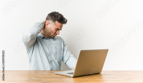 Young handsome man working with his laptop suffering neck pain due to sedentary lifestyle.