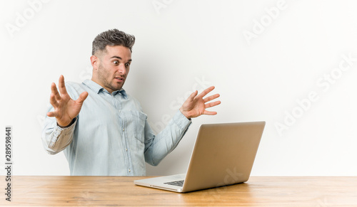 Young handsome man working with his laptop being shocked due to an imminent danger