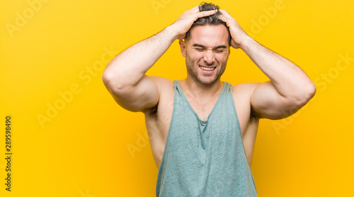 Young fitness man against a yellow background laughs joyfully keeping hands on head. Happiness concept.