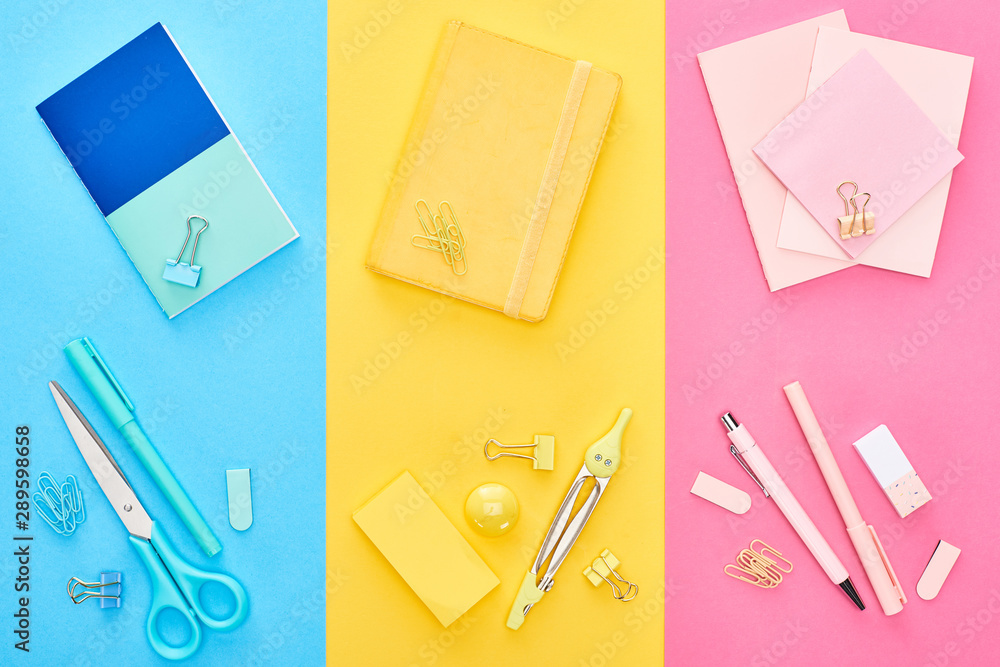 Top view of yellow and blue notepads near pink sheets of paper with different stationery on tricolor background Top view of yellow and blue notepads near pink sheets of paper with different stationery on tricolor background