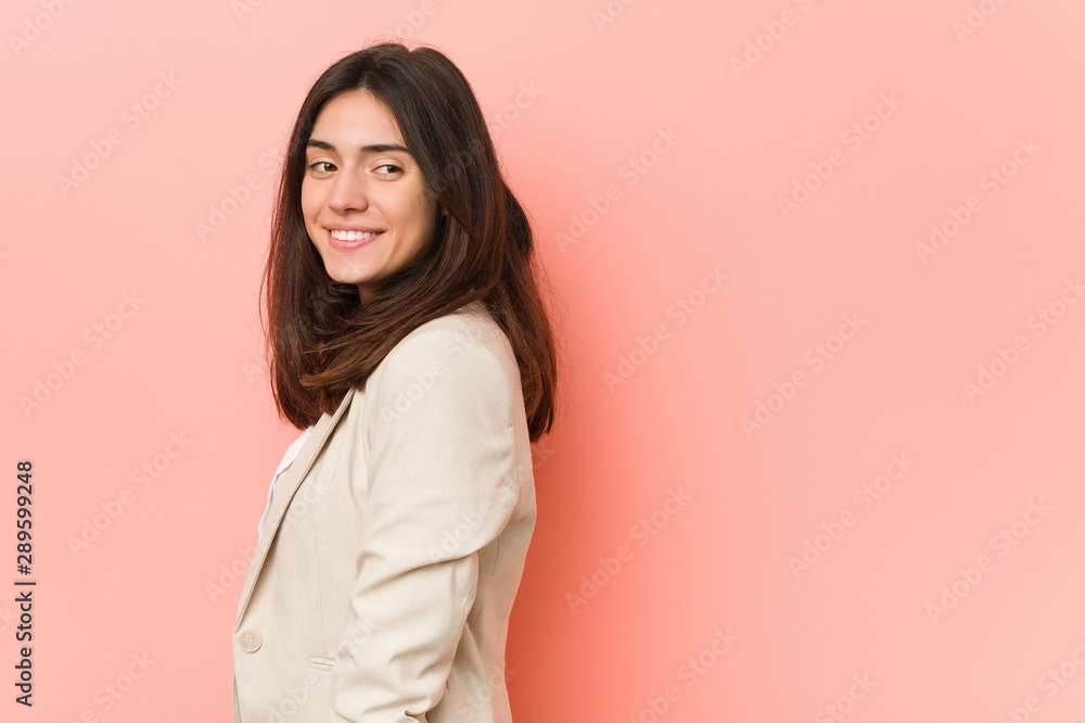 Fototapeta premium Young brunette business woman against a pink background looks aside smiling, cheerful and pleasant.