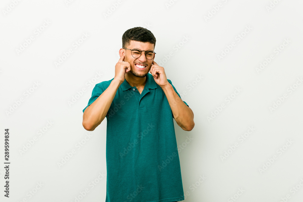 Young hispanic man covering ears with hands.