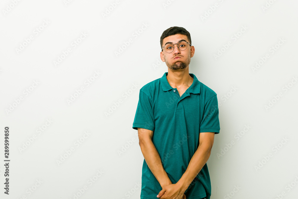 Fototapeta premium Young hispanic man blows cheeks, has tired expression. Facial expression concept.