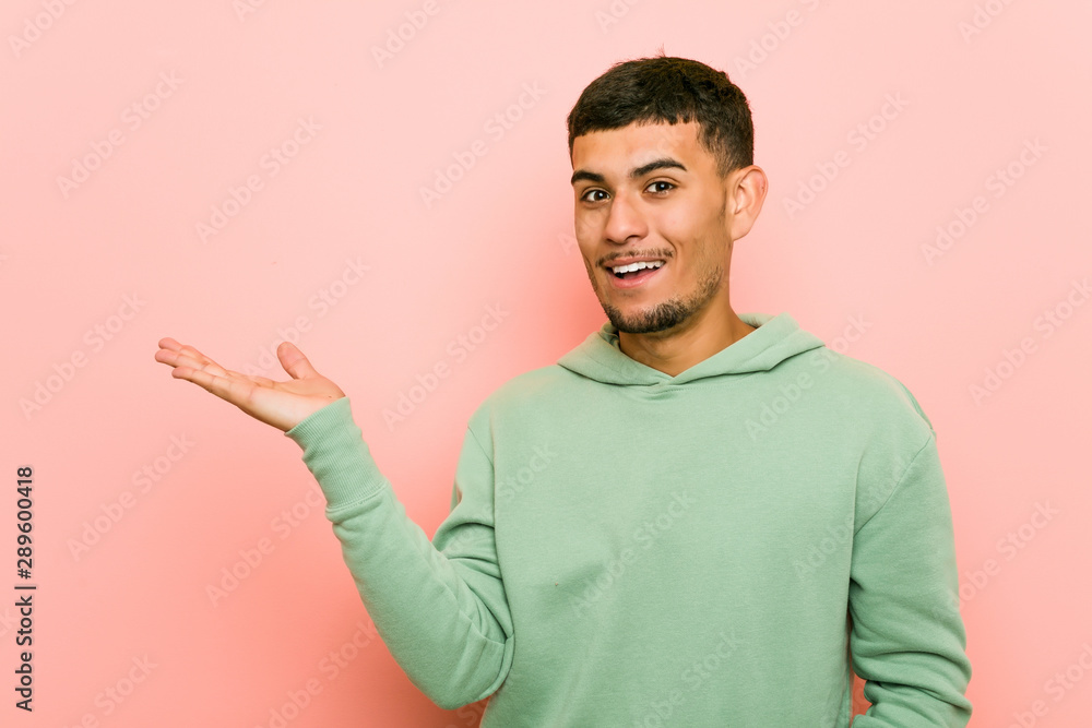 Young hispanic sport man holds copy space on a palm, keep hand over cheek. Amazed and delighted. Young hispanic sport man holds copy space on a palm, keep hand over cheek. Amazed and delighted.
