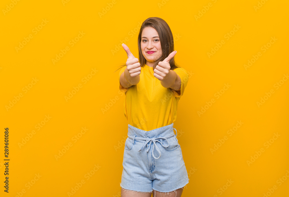 Young woman teenager wearing a yellow shirt with thumbs ups, cheers about something, support and respect concept. Young woman teenager wearing a yellow shirt with thumbs ups, cheers about something, support and respect concept.