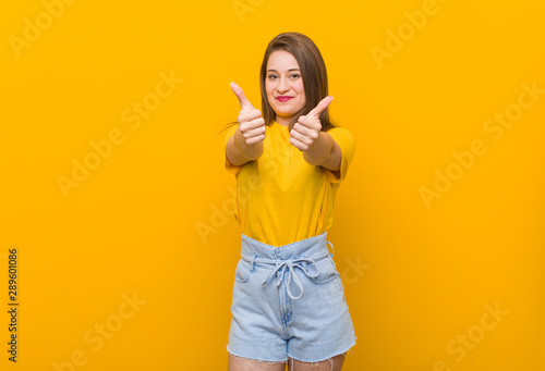Young woman teenager wearing a yellow shirt with thumbs ups, cheers about something, support and respect concept.