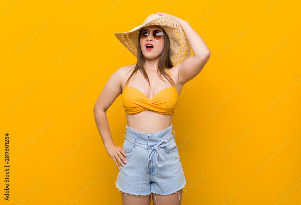 Young caucasian woman wearing a straw hat, summer look tired and very sleepy keeping hand on head.