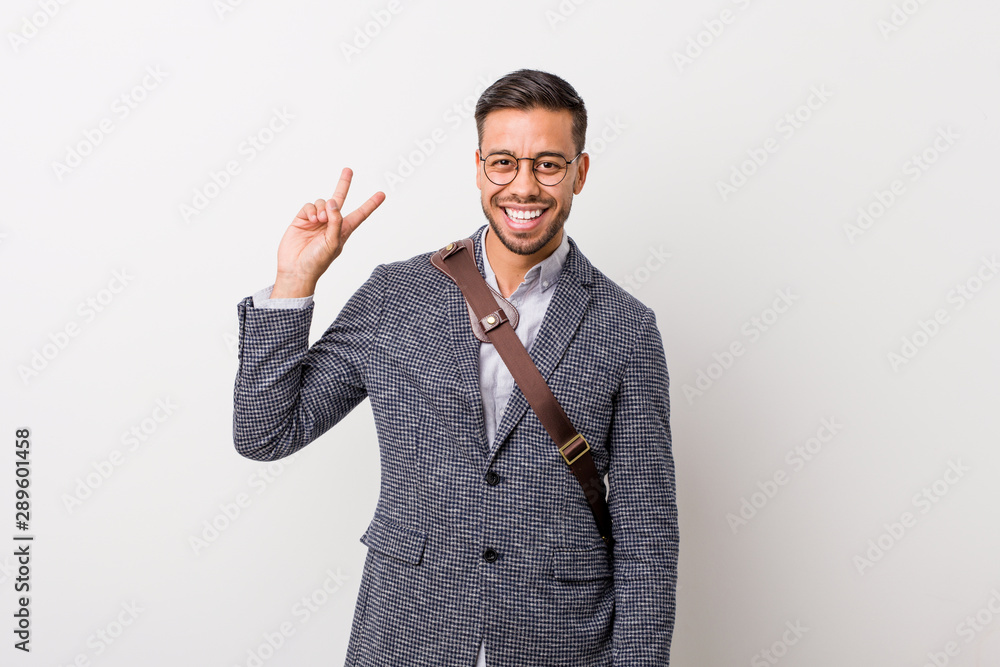 Young business filipino man against a white wall joyful and carefree showing a peace symbol with fingers. Young business filipino man against a white wall joyful and carefree showing a peace symbol with fingers.