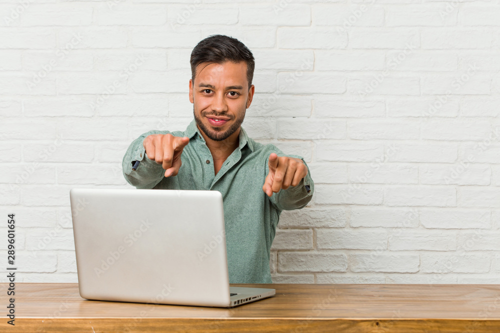 Young filipino man sitting working with his laptop cheerful smiles pointing to front. Young filipino man sitting working with his laptop cheerful smiles pointing to front.