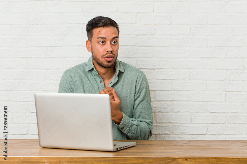 Young filipino man sitting working with his laptop scared and afraid. Young filipino man sitting working with his laptop scared and afraid.