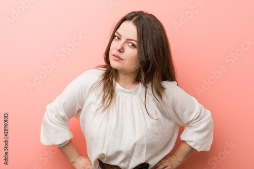 Young caucasian curvy woman standing against pink background