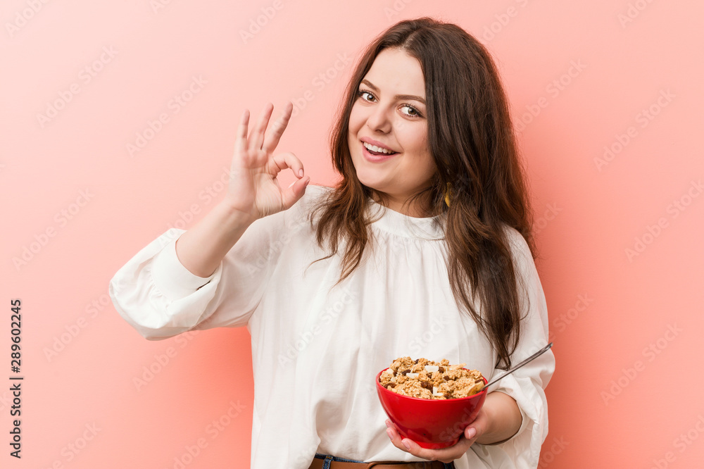 Young plus size curvy woman holding a cereals bowl cheerful and confident showing ok gesture. Young plus size curvy woman holding a cereals bowl cheerful and confident showing ok gesture.