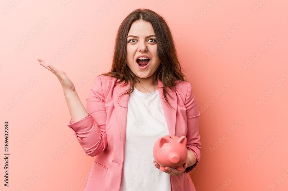 Young plus size curvy business woman holding a piggy bank celebrating a victory or success Young plus size curvy business woman holding a piggy bank celebrating a victory or success