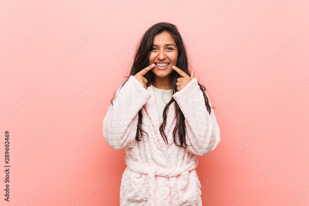 Young indian woman wearing pajama smiles, pointing fingers at mouth. Young indian woman wearing pajama smiles, pointing fingers at mouth.
