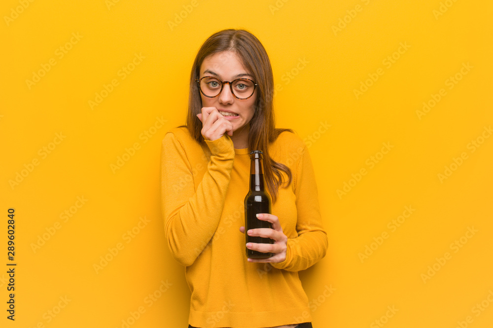 Young pretty caucasian woman biting nails, nervous and very anxious. She is holding a beer. Young pretty caucasian woman biting nails, nervous and very anxious. She is holding a beer.