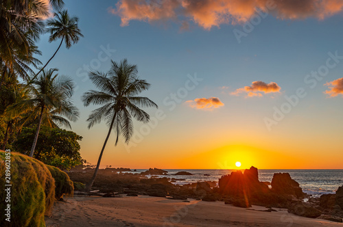 Fototapeta Naklejka Na Ścianę i Meble -  Sunset along the volcanic rock beach of Corcovado national park with a sunbeam by the Pacific Ocean, Costa Rica, Central America.
