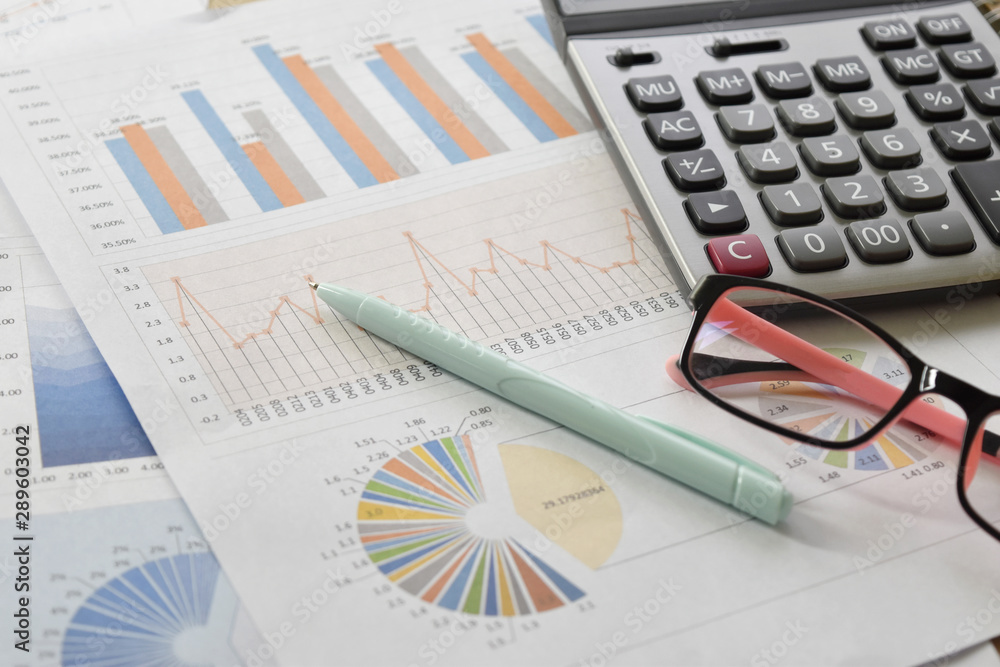 Obraz premium Financial graphs and charts with glasses, calculator on desk.