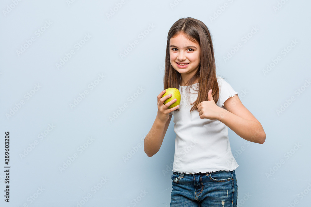Little caucasian girl holding a green apple smiling and raising thumb up Little caucasian girl holding a green apple smiling and raising thumb up