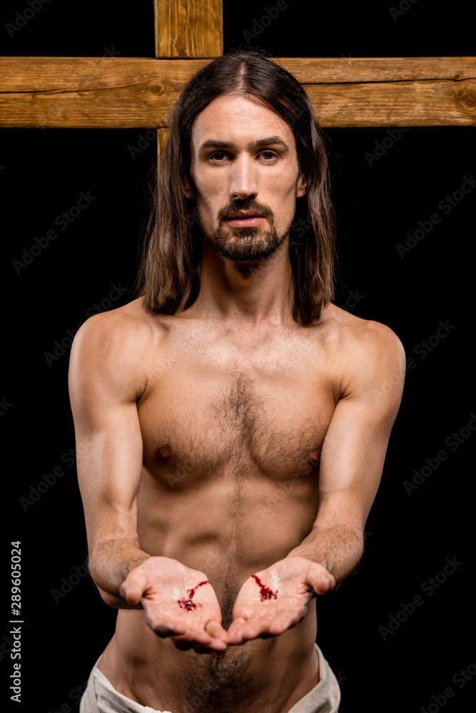 jesus with bloody hands standing near wooden cross isolated on black