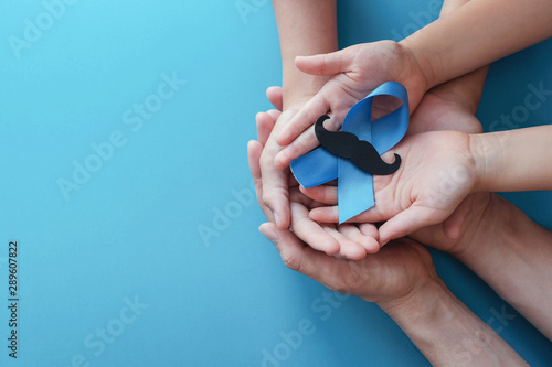 Family hands holding light blue ribbonwith mustache on blue background , Prostate Cancer Awareness, Men health awareness, November Blue
