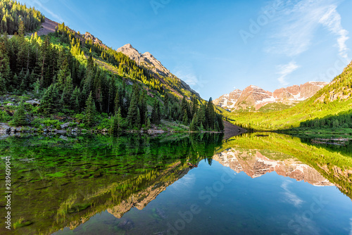 Maroon Bells lake at sunrise wide angle view in Aspen, Colorado with rocky mountain peak and snow in July 2019 summer and vibrant light reflection on water